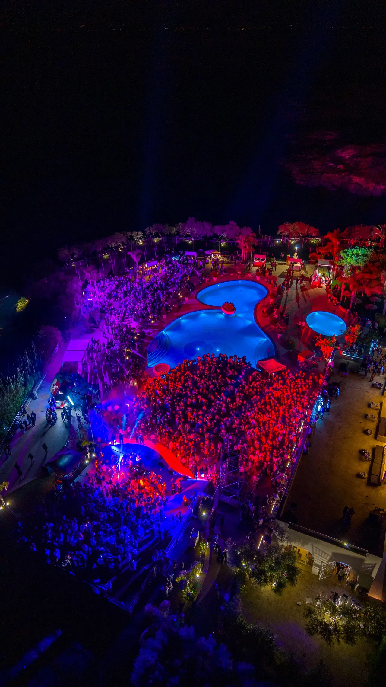 La festa di notte vista dall’alto, luci viola e piscine illuminate