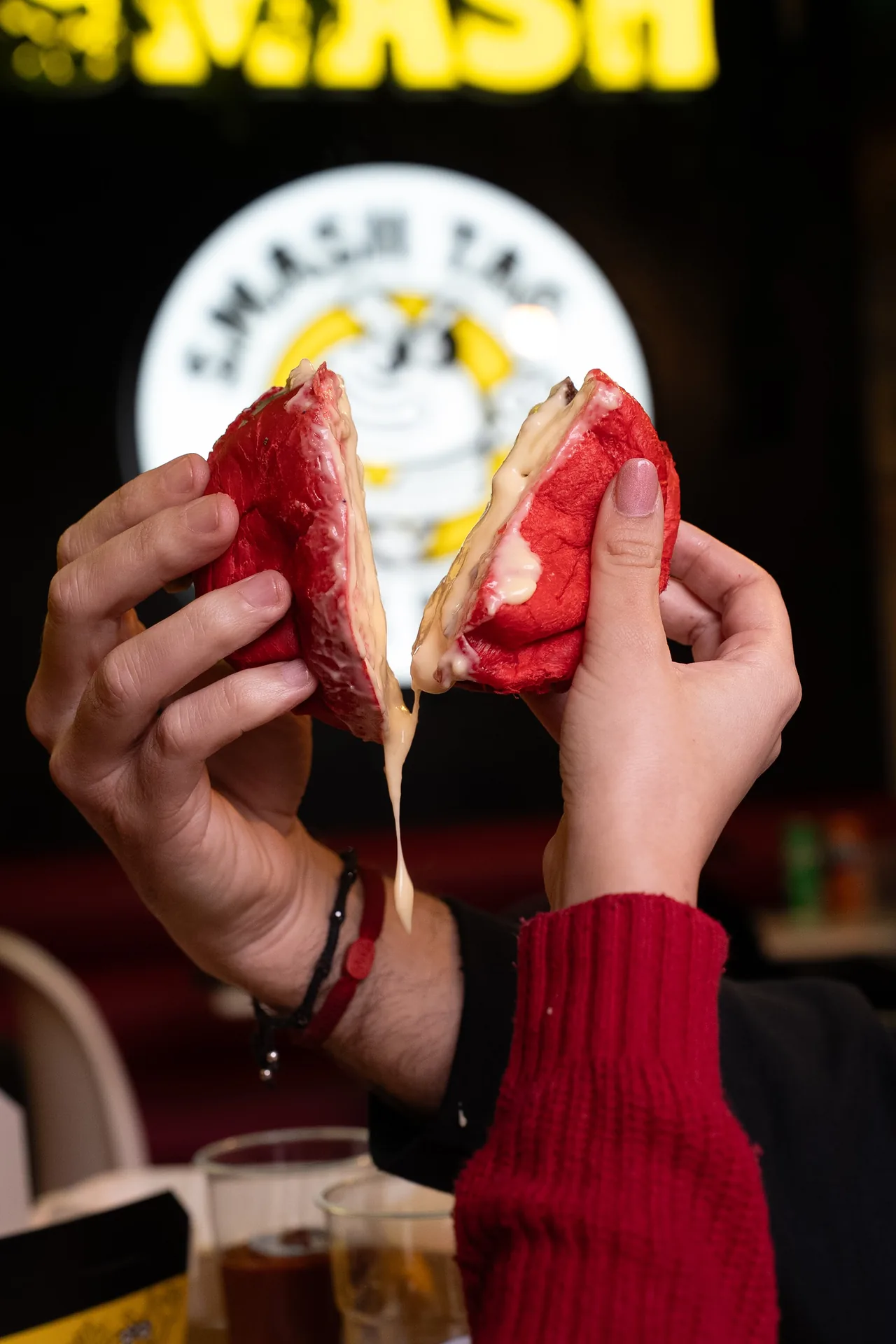 Mani che aprono uno smash burger rosso davanti all’insegna Smash Tag