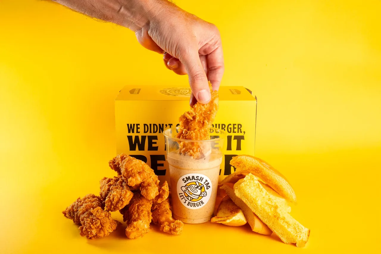 Chicken tender, patatine e shake davanti al box Smash Tag su fondo giallo