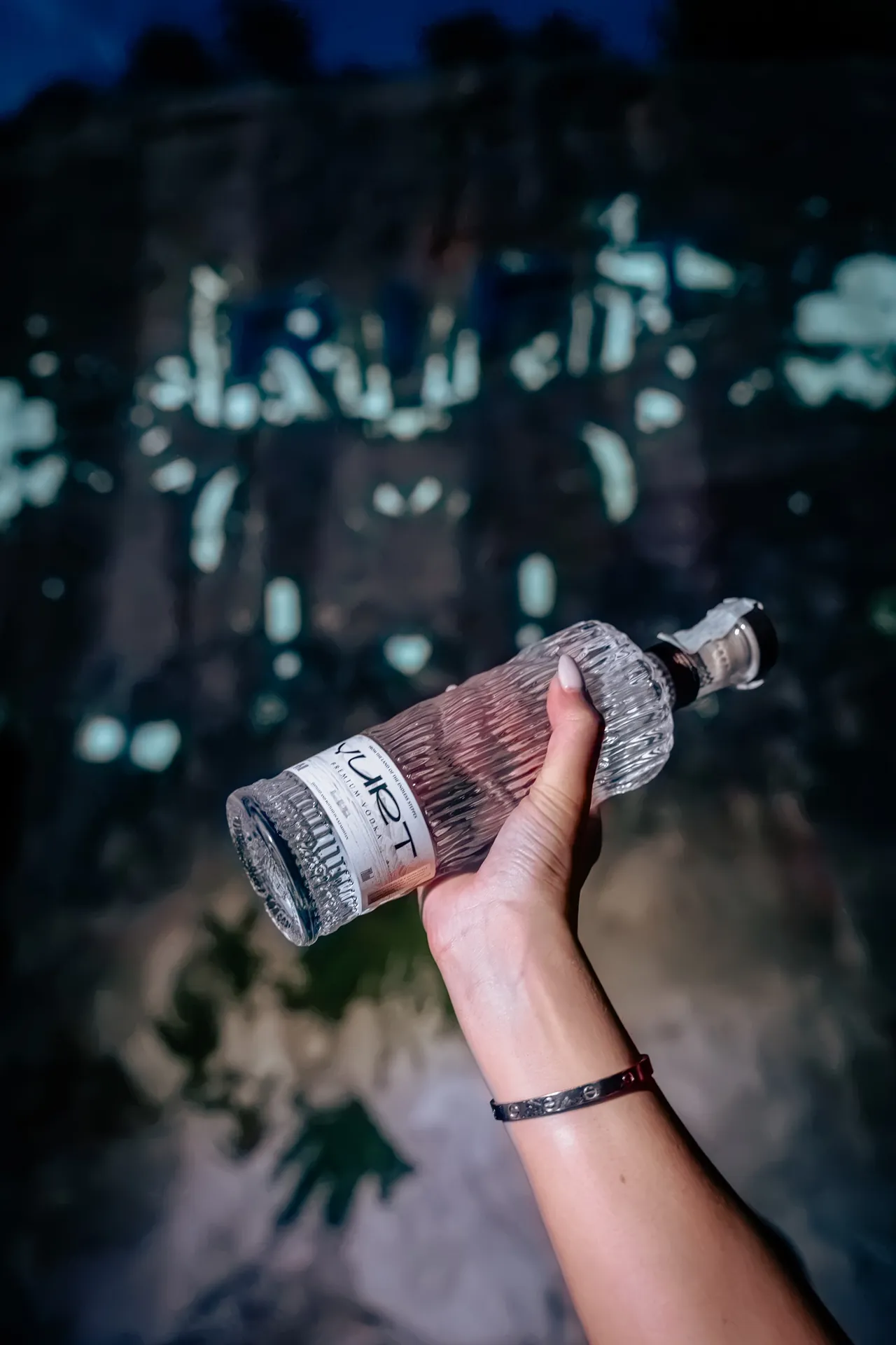 Una bottiglia di Yurt Vodka alzata davanti alla parete della cava illuminata di blu